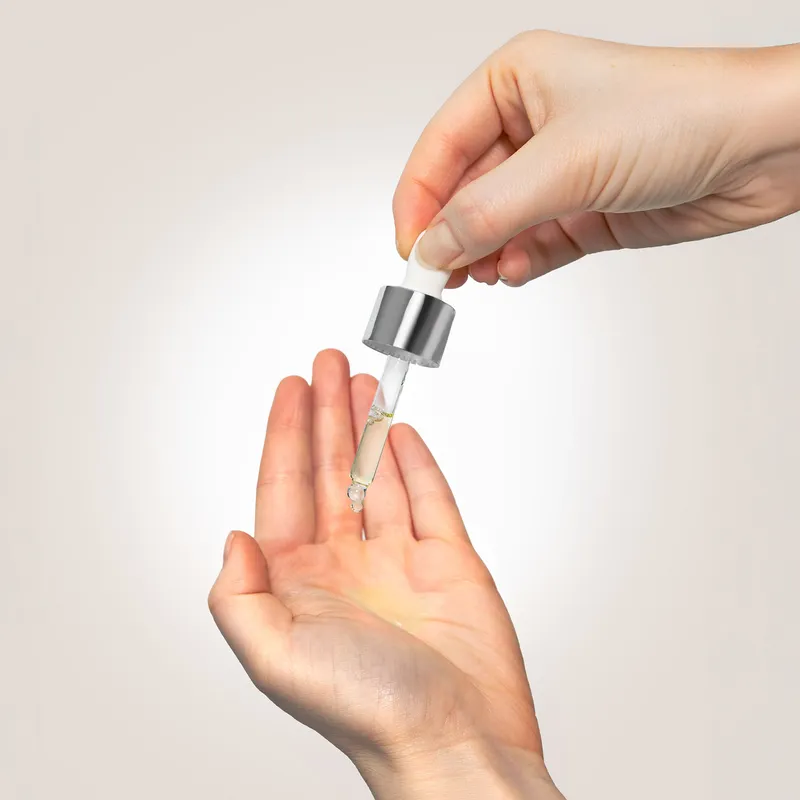 A dropper releasing a few drops of facial oil into an open palm.