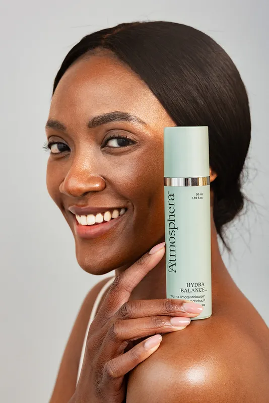 A smiling woman holding a bottle of HYDRA BALANCE™ against her cheek.